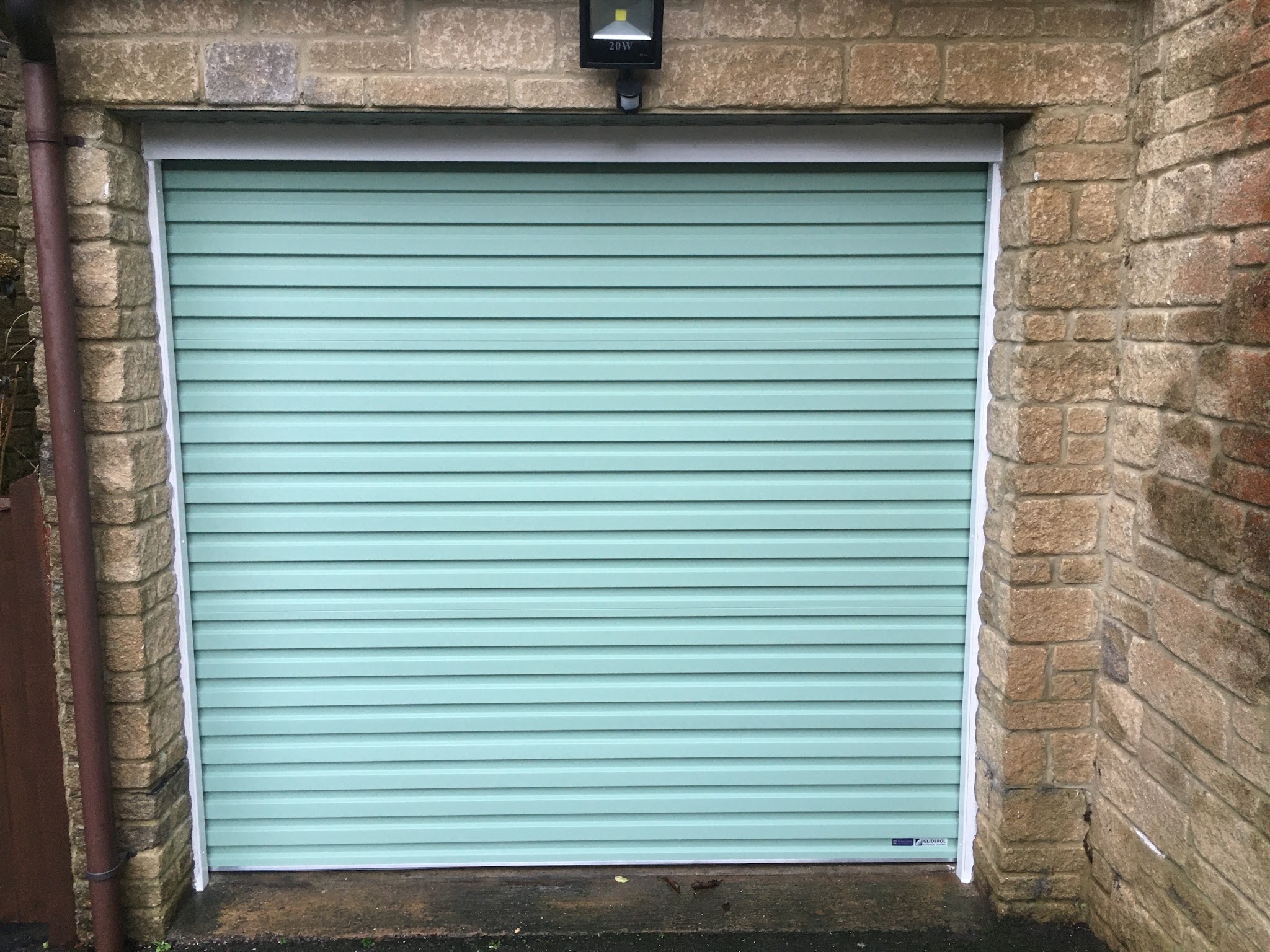 Sage green roller garage door fitted in a stone garage